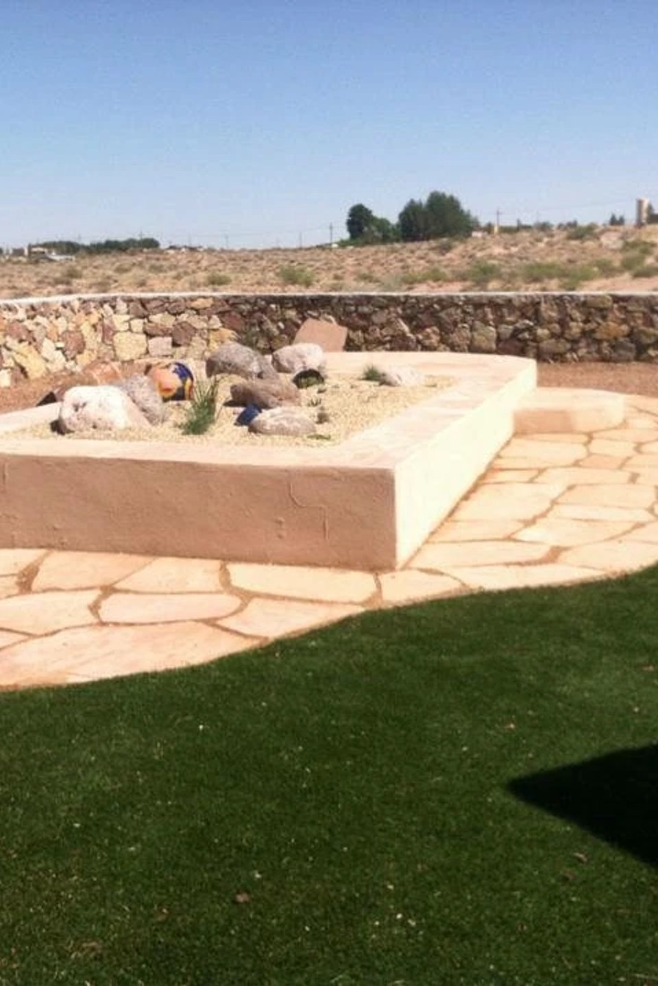 Flagstone patio with raised stone planter and lush turf installed by Brainard's Greenscapes
