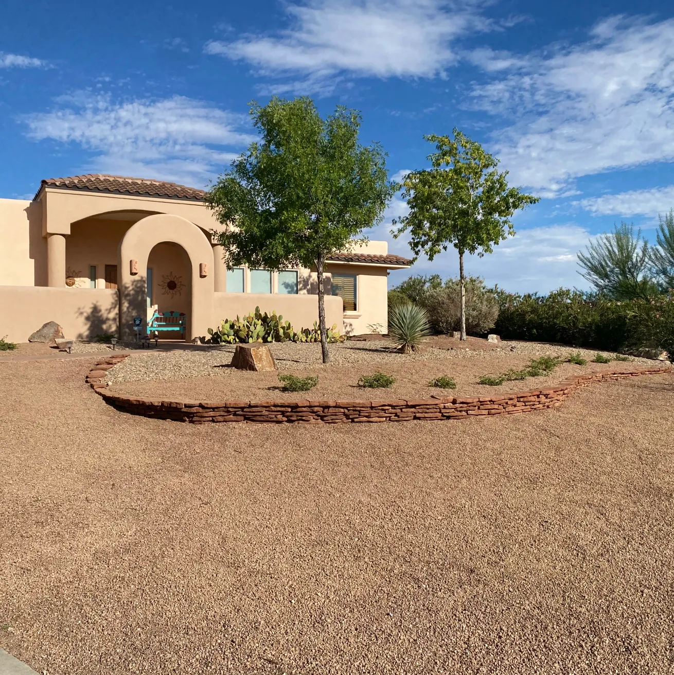 Curving dry-stack stone border defining a planting bed in front of a Pueblo-style adobe home in Las Cruces