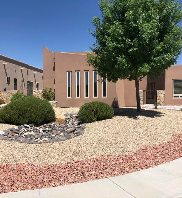 Pueblo-style home framed by a stone-bordered xeriscape with shrubs and dry creek