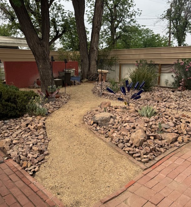 Backyard xeriscape combining brick patio, river-rock beds, and garden art